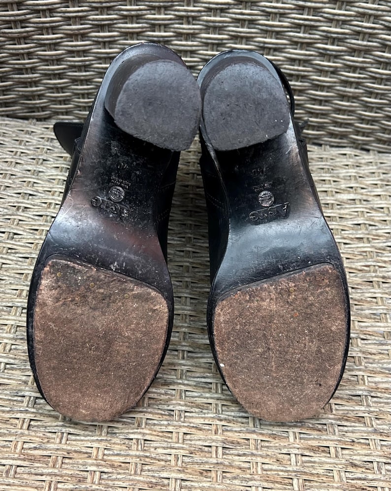 May include: A pair of black leather ankle boots with block heels. The soles are worn, showing signs of use. The heels are approximately 3 inches high. The boots are set against a woven background.