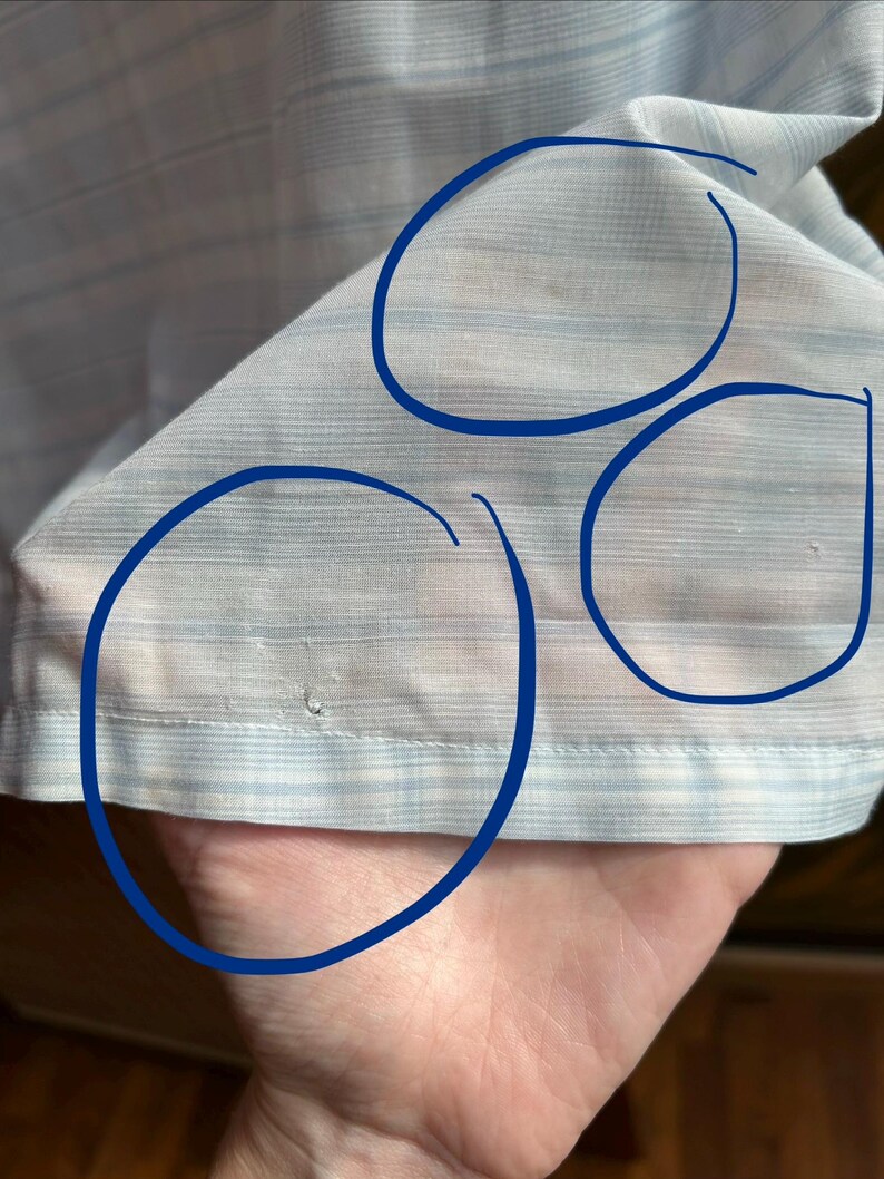 May include: A light blue and white striped fabric garment featuring three blue circles drawn on the surface to highlight small areas of discoloration and a tiny hole near the bottom hem of the material.