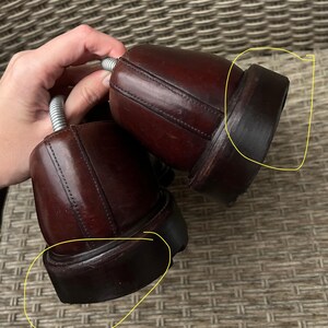 May include: Pair of dark brown leather dress shoes with stacked heels. The shoes are in good condition and appear to be well-maintained. The image shows the back of the shoes, highlighting the heel and sole construction. The shoes are likely for formal or business attire.
