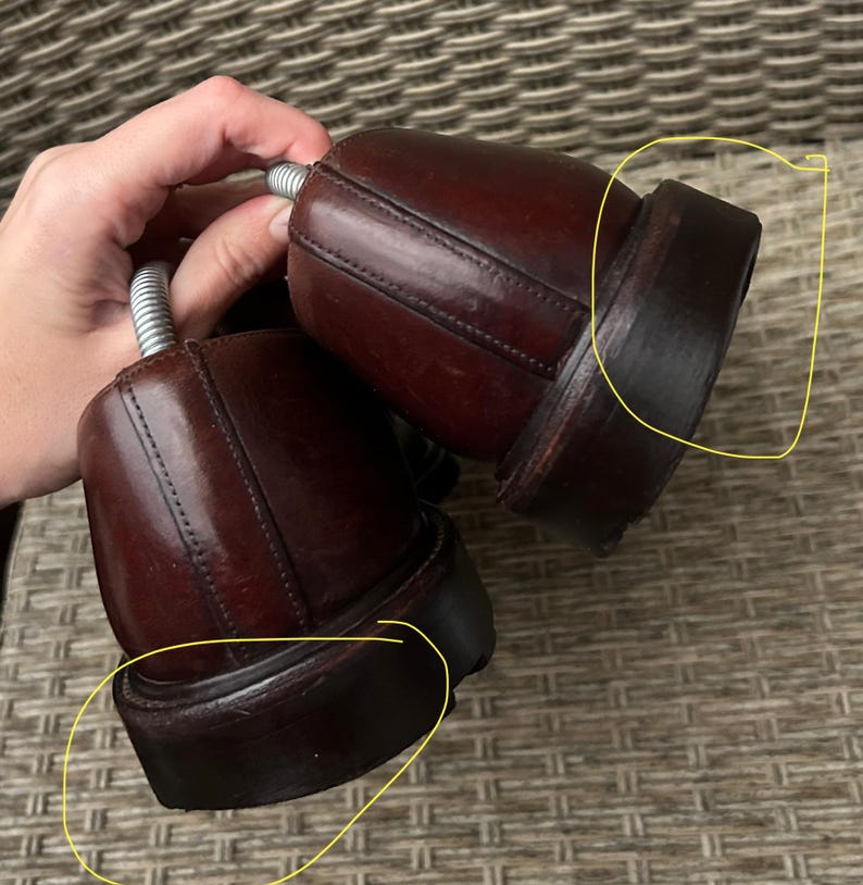 May include: Pair of dark brown leather dress shoes with stacked heels. The shoes are in good condition and appear to be well-maintained. The image shows the back of the shoes, highlighting the heel and sole construction. The shoes are likely for formal or business attire.