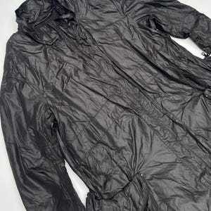 May include: Black, long, quilted jacket with a high collar and a zipper closure. The jacket has multiple pockets and a drawstring waist. The material has a slight sheen. The jacket is designed for outdoor wear.
