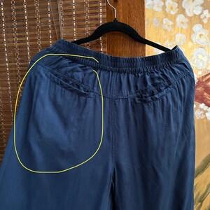 May include: Navy blue wide-leg trousers hanging on a black hanger. The trousers have a drawstring waist and two pockets on the back. The fabric appears to be lightweight and flowing.