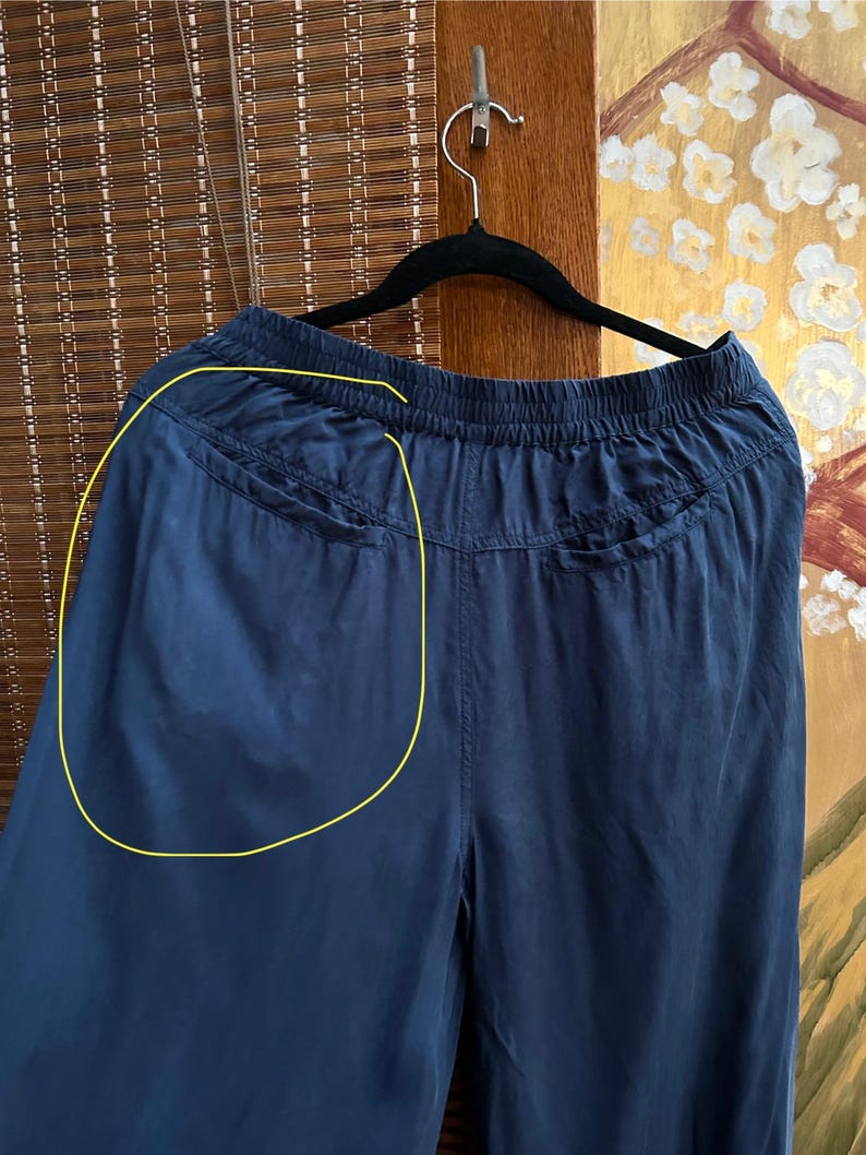 May include: Navy blue wide-leg trousers hanging on a black hanger. The trousers have a drawstring waist and two pockets on the back. The fabric appears to be lightweight and flowing.