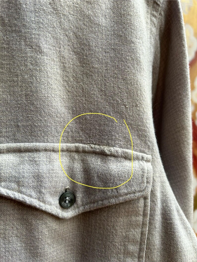 以下が含まれることがあります： ベージュのボタンダウンシャツのクローズアップ。 シャツには、ボタン留めのシングルポケットが付いています。 生地は質感のある外観です。