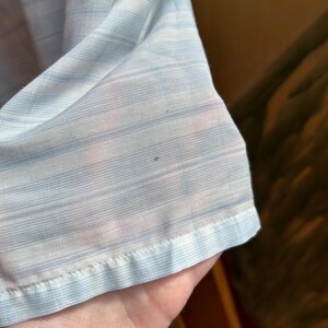 May include: A lightweight, semi-sheer fabric featuring a pattern of thin, horizontal light blue and white stripes. The material has a visible, fine-textured weave and a finished hem along the bottom edge, showing a small dark spot on the surface.