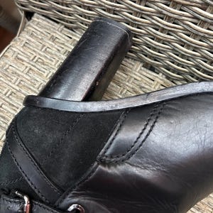 May include: Close-up of a black leather boot with a block heel. The boot features a suede panel and decorative stitching. The heel is approximately 3 inches high. The leather appears to be smooth and well-maintained.