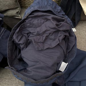 May include: Navy blue drawstring trousers with an elasticated waistband. The trousers are made of a lightweight fabric and have a relaxed fit. The interior lining is a darker shade of navy blue. The trousers are folded, showing the interior and exterior.