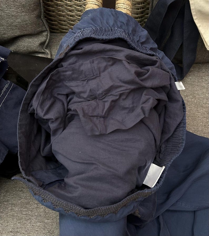 May include: Navy blue drawstring trousers with an elasticated waistband. The trousers are made of a lightweight fabric and have a relaxed fit. The interior lining is a darker shade of navy blue. The trousers are folded, showing the interior and exterior.