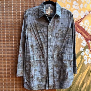 May include: A button-down shirt with a tropical palm tree print in shades of gray, brown, and red. The shirt has long sleeves, two chest pockets, and a collar. The shirt is hanging on a black hanger.