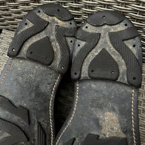 May include: Close-up of the soles of two black leather shoes. The soles have a textured, patterned design with the words "Ridgeway" and "Made in England" visible. The shoes appear worn.