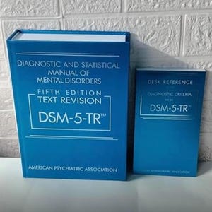 Könnte beinhalten: Zwei blaue Bücher, eines groß und eines klein, mit weißem Text. Das größere Buch lautet "Diagnostic and Statistical Manual of Mental Disorders, Fifth Edition, Text Revision, DSM-5-TR". Das kleinere Buch ist eine "Desk Reference" mit "DSM-5-TR".