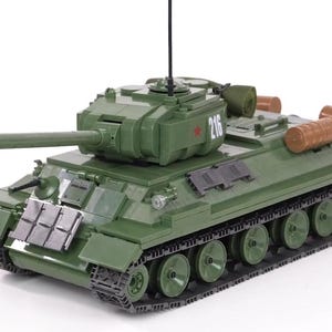 Può includere: Un carro armato giocattolo verde con un tronco di legno marrone sul retro. Il carro armato ha una stella rossa e il numero 216 sul lato.