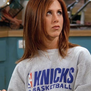 May include: A light gray crewneck sweatshirt featuring the blue text KNICKS BASKETBALL and the red, white, and blue NBA logo printed on the front. The garment has long sleeves and a ribbed neckline, constructed from a heathered fabric material.