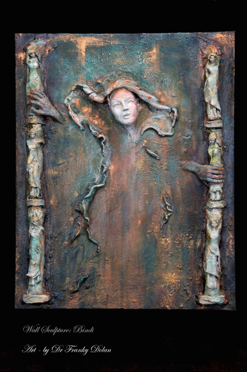 May include: A textured, green, brown, and gold wall sculpture with a central figure of a woman with a flowing white cloth. The sculpture is framed by two columns with figures on them. The text "Wall Sculpture: Bindi Art - by Dr Franky Dolan" is at the bottom of the image.
