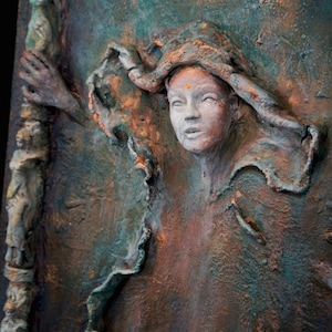 May include: A textured, three-dimensional painting of a woman's face with a gold dot on her forehead. The woman is wearing a textured, flowing garment. The background is a mix of green, brown, and gold colors.