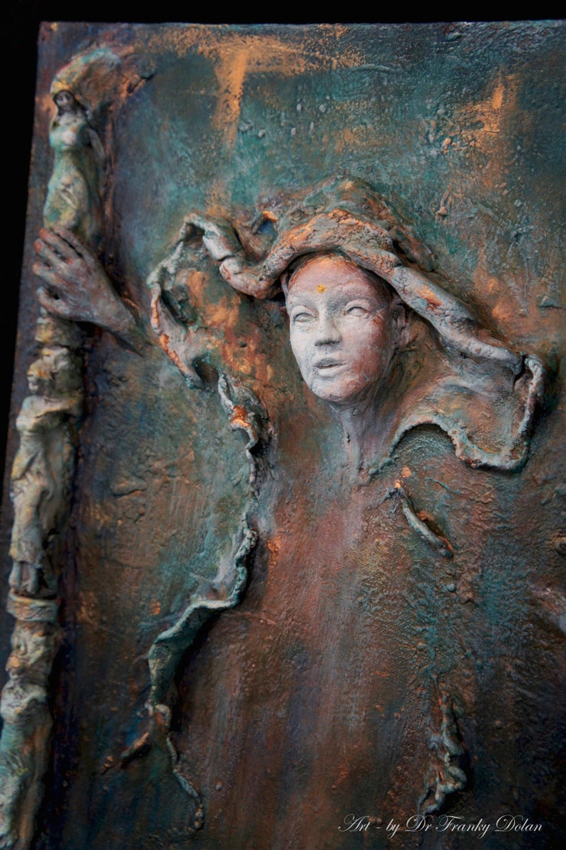 May include: A textured, three-dimensional painting of a woman's face with a gold dot on her forehead. The woman is wearing a textured, flowing garment. The background is a mix of green, brown, and gold colors.