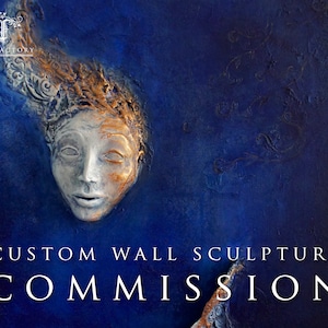 May include: Custom wall sculpture commission. A 3D relief sculpture of a face with gold and white paint on a dark blue background.