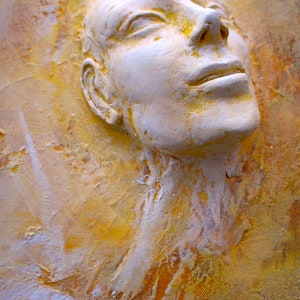 May include: A white plaster sculpture of a face with closed eyes and a slightly open mouth, set against a yellow and orange textured background.