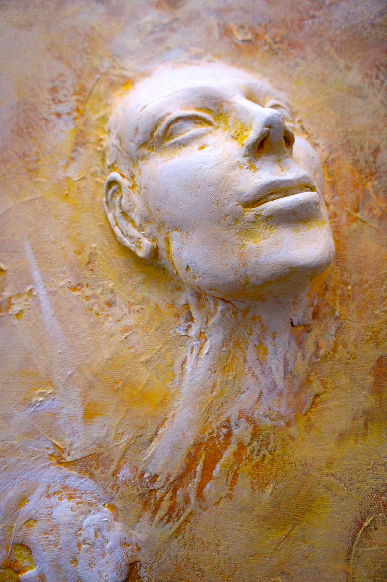 May include: A white plaster sculpture of a face with closed eyes and a slightly open mouth, set against a yellow and orange textured background.