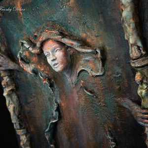 May include: A textured, three-dimensional artwork featuring a woman's face with a copper and green color scheme. The woman's face is partially obscured by a textured, flowing fabric. The artwork is set against a dark background.