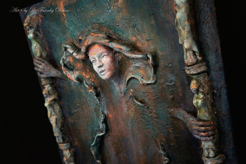May include: A textured, three-dimensional artwork featuring a woman's face with a copper and green color scheme. The woman's face is partially obscured by a textured, flowing fabric. The artwork is set against a dark background.