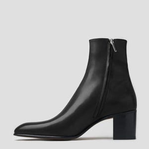 Puede incluir: Botines de cuero negro con cremallera lateral y tacón cuadrado. Los botines tienen punta afilada y un acabado liso. El tacón mide aproximadamente 6,35 cm de alto.