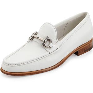 May include: White leather loafer with a silver-tone metal buckle detail. The shoe has a rounded toe, a low heel, and a stitched design around the edges. The sole is a light brown color.