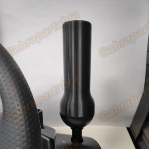 Puede incluir: Una extensión de palanca de cambios de plástico negro para un volante de carreras. La extensión está diseñada para ser añadida a la parte superior de una palanca de cambios estándar.