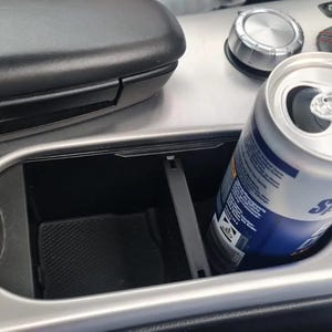 Könnte beinhalten: Ein silberner Getränkehalter im Auto mit einer blauen und weißen Dose Limonade darin. Die Dose ist teilweise sichtbar und die Oberseite der Dose ist offen.