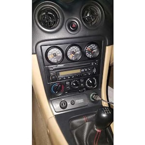 May include: A black dashboard with a radio, gauges, and a gear shifter. The dashboard is beige and has a red stitching detail.