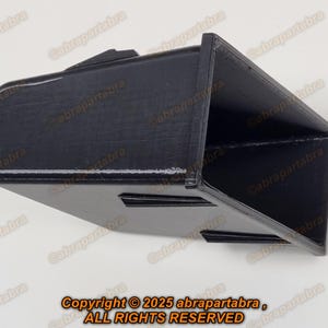 May include: A black plastic car part with a rectangular shape and a textured surface. The part has a small opening on one side.