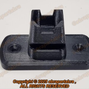 Puede incluir: Un objeto negro impreso en 3D con una base rectangular y un componente vertical en forma de U. La base tiene bordes redondeados y dos hendiduras circulares. El texto "Copyright © 2025 abrapartabra, ALL RIGHTS RESERVED" es visible.
