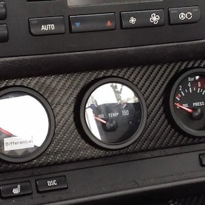 Puede incluir: Primer plano del salpicadero de un coche con tres indicadores. Los indicadores están etiquetados como "Diferencial", "Temp. aceite" y "Presión aceite". El salpicadero está hecho de fibra de carbono.