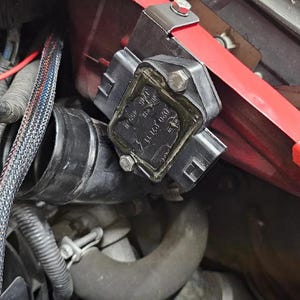 May include: An engine component assembly featuring a black sensor with the number "020 971 11" visible. The assembly is mounted on a red metal frame with a black bracket and bolts. Hoses and wiring are also present.