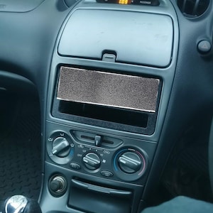 Puede incluir: Un interior de coche gris con un reloj digital que muestra la 1:09, un espacio en blanco donde estaría la radio y una fila de botones de control del clima.