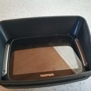 May include: A black TomTom GPS navigation device with a screen inside a black protective case.