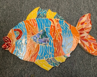 May include: A mosaic fish sculpture with blue, orange, yellow, and red tiles. The fish has a large, open mouth and a long, flowing tail.