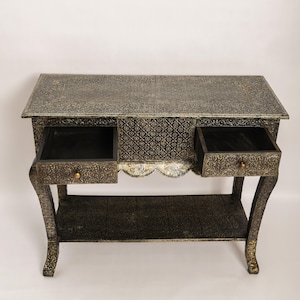 Könnte beinhalten: Antik-Konsole mit zwei offenen Schubladen. Der Tisch hat ein detailliertes, geprägtes Muster in Schwarz und Gold. Die Schubladen haben Messingknöpfe und die Beine sind geschwungen. Abmessungen: ca. 100 cm lang.