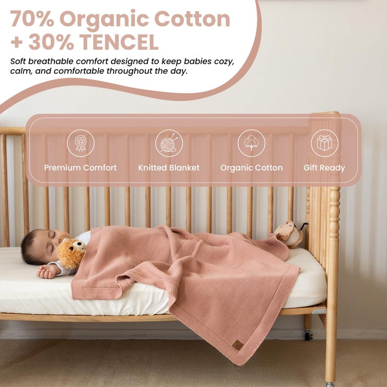 Może przedstawiać: Dziecko śpi spokojnie pod miękkim, r&oacute;żowym, dzianinowym kocem w drewnianym ł&oacute;żeczku. Koc wykonany jest w 70% z bawełny organicznej i 30% TENCEL. Obraz zawiera tekst "Premium Comfort", "Knitted Blanket", "Organic Cotton" i "Gift Ready".