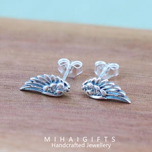 May include: A pair of silver angel wing earrings with clear cubic zirconia stones. The earrings are on a wooden surface.