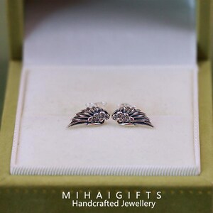 May include: A pair of silver earrings with a wing design and small clear stones. The earrings are in a white box with a green lid.