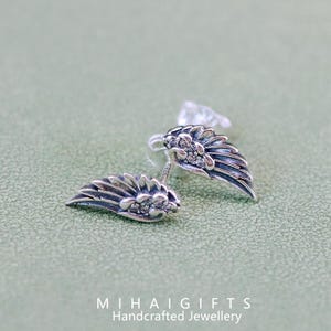 May include: A pair of silver earrings with a wing design and clear crystal accents. The earrings are small and delicate.