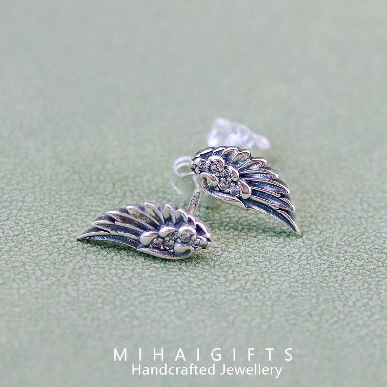 May include: A pair of silver earrings with a wing design and clear crystal accents. The earrings are small and delicate.