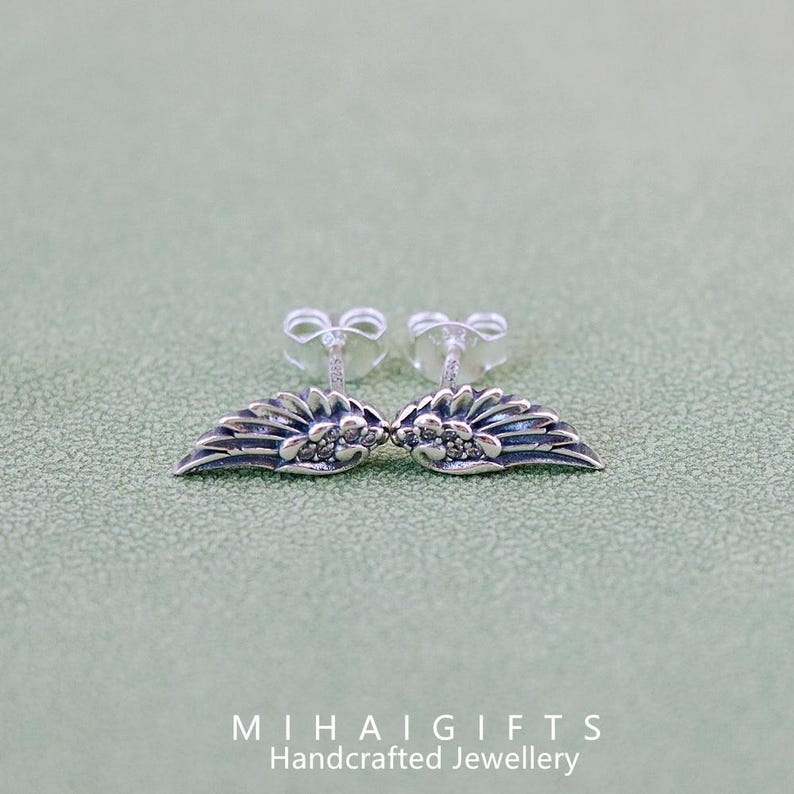May include: A pair of silver earrings with a wing design and small clear stones.