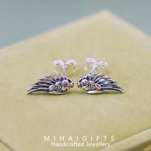May include: A pair of silver angel wing earrings with small clear cubic zirconia stones. The earrings are on a green velvet background.