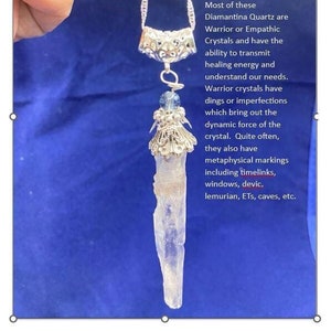May include: A silver necklace with a clear quartz crystal pendant. The crystal has a natural, rough texture and is attached to a silver chain with a decorative silver clasp. The text "Diamantina Singing Quartz Crystals - mined in the 1990s. Carry an intense vibration with deep focused energy. Most of these Diamantina Quartz are Warrior or Empathic Crystals and have the ability to transmit healing energy and understand our needs. Warrior crystals have dings or imperfections which bring out the dynamic force of the crystal. Quite often, they also have metaphysical markings including timelinks, windows, devic, lemurian, ETs, caves, etc." is visible in the image.