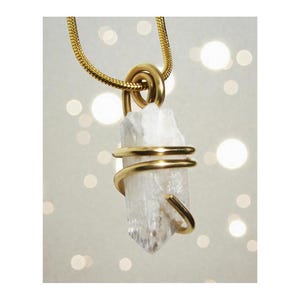 May include: A gold-coloured necklace with a clear, rough-cut crystal pendant. The crystal is wrapped with a spiral of gold-coloured wire. The necklace chain is also gold-coloured.
