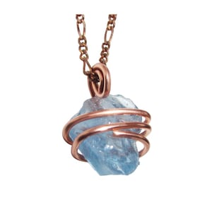 May include: A light blue, raw gemstone pendant wrapped in copper wire, suspended from a copper chain. The gemstone is a rough, irregular shape. The copper wire is coiled around the stone, creating a cage-like design. The chain is a delicate, linked style.