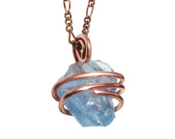 May include: A light blue, raw gemstone pendant wrapped in copper wire, suspended from a copper chain. The gemstone is a rough, irregular shape. The copper wire is coiled around the stone, creating a cage-like design. The chain is a delicate, linked style.