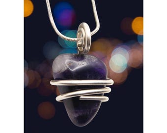 May include: A silver chain necklace with a purple amethyst stone wrapped in silver wire. The stone is heart-shaped and has a natural, rough texture.